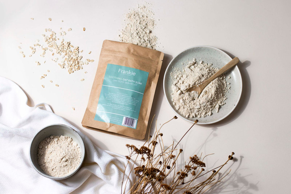 Frankie Apothecary Soothing Oat Bath Soak pouch with finely milled colloidal oatmeal on a speckled plate and in a ceramic bowl, rolled oats scattered beside it